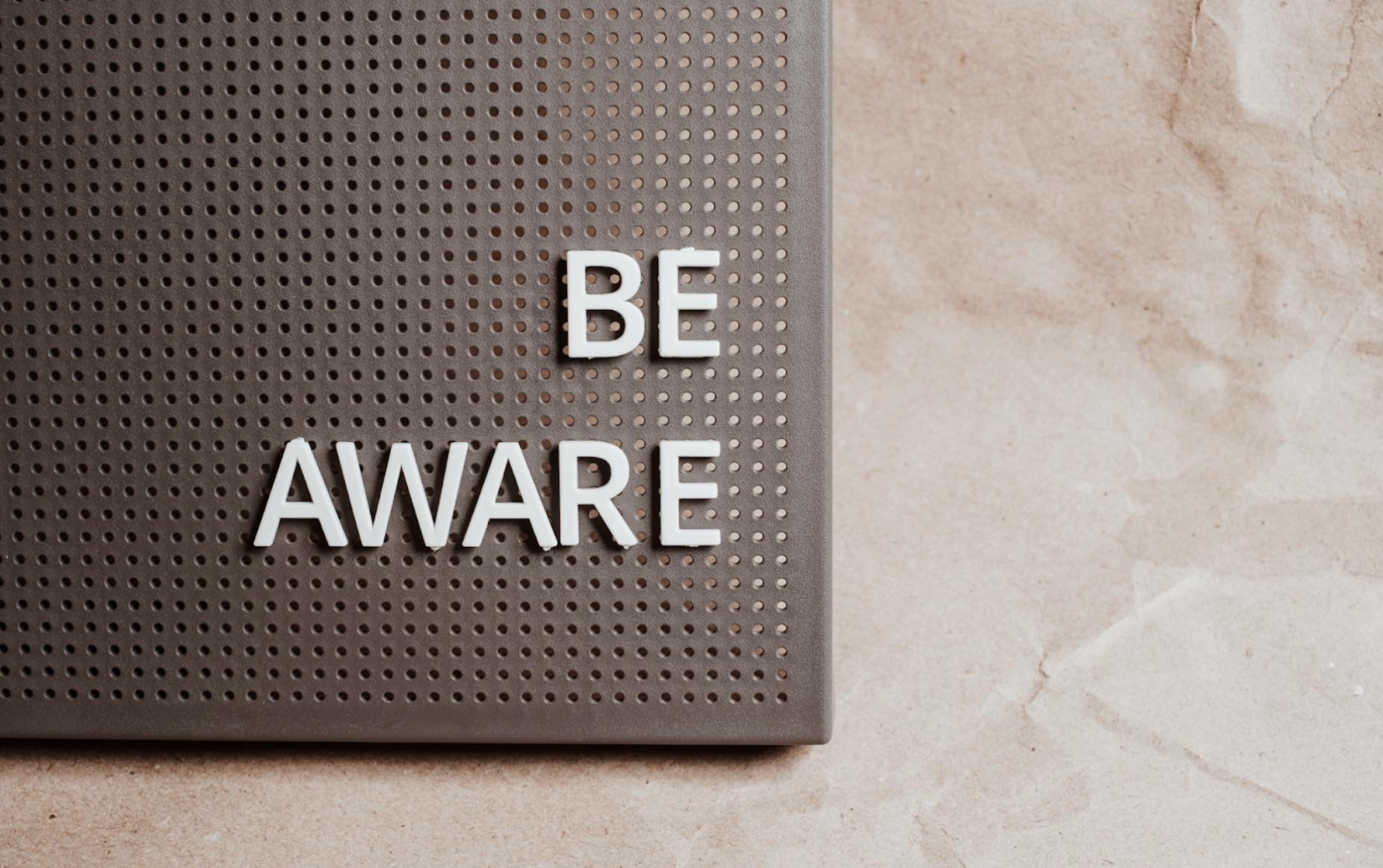 Text 'Be Aware' displayed on a perforated surface, emphasizing the importance of staying informed about tax forms.